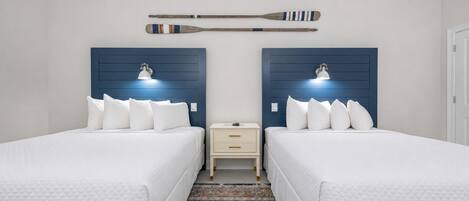 A hotel room with two beds, a nightstand, a wall-mounted lamp, and a decorative wall piece.