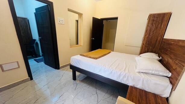 A bedroom with a bed, a wooden headboard, a mirror, and a door leading to another room. - Aashira Residency (Mayiladuthurai)
