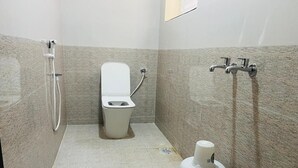 A small bathroom with a toilet, a shower, and a hand dryer. - Aashira Residency (Mayiladuthurai)