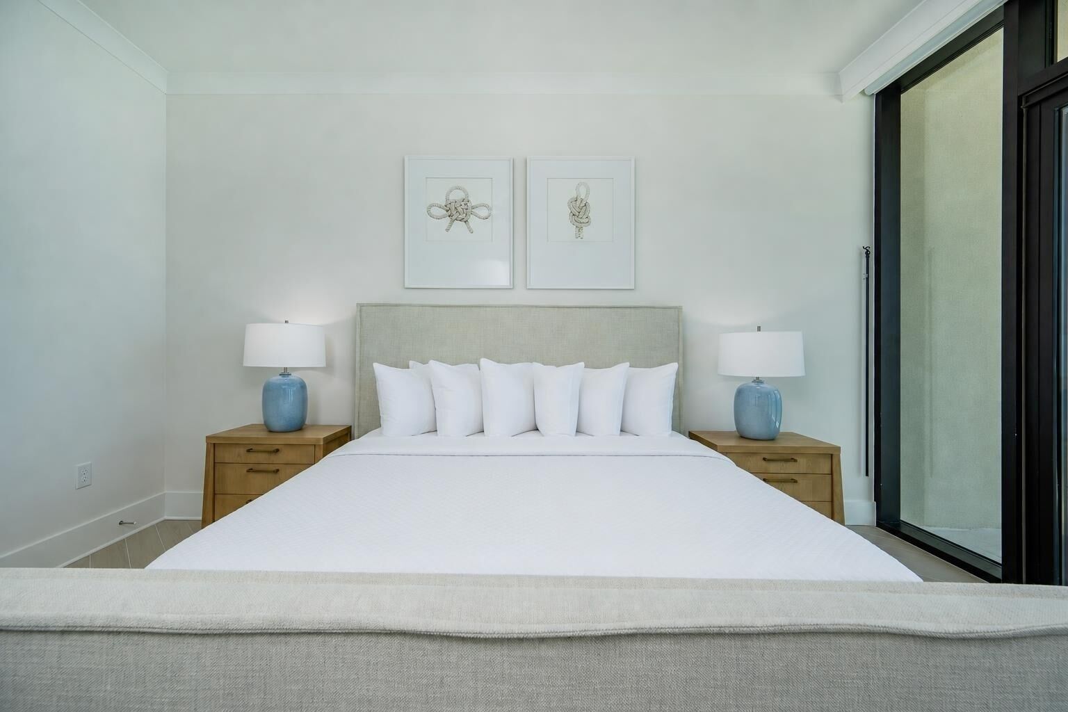 A bedroom with a large bed, two bedside tables with lamps, and two framed artworks on the wall.