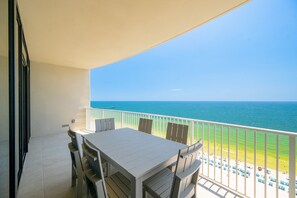 A balcony with a view of the sea, a table, and chairs.