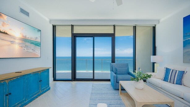 A modern living room with a large sliding glass door leading to a balcony with a view of the ocean. - Phoenix Gulf Shores Ii 1702 3 Bedroom Condo (Gulf Shores)