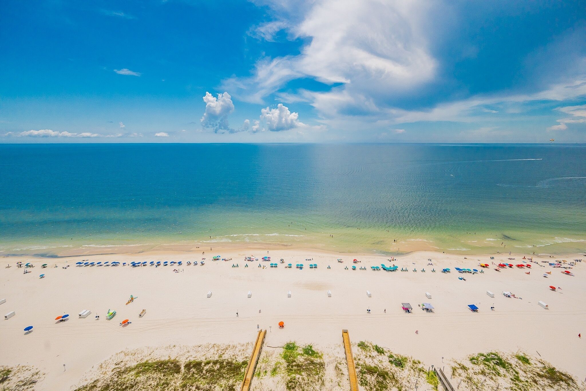 A beach with numerous umbrellas and sun loungers, a clear sky, and calm waters.