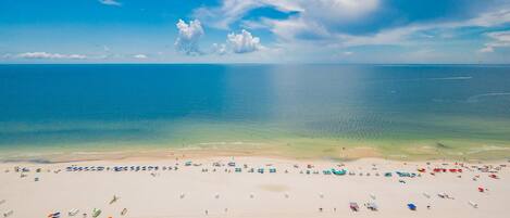 A beach with numerous umbrellas and sun loungers, a clear sky, and calm waters.
