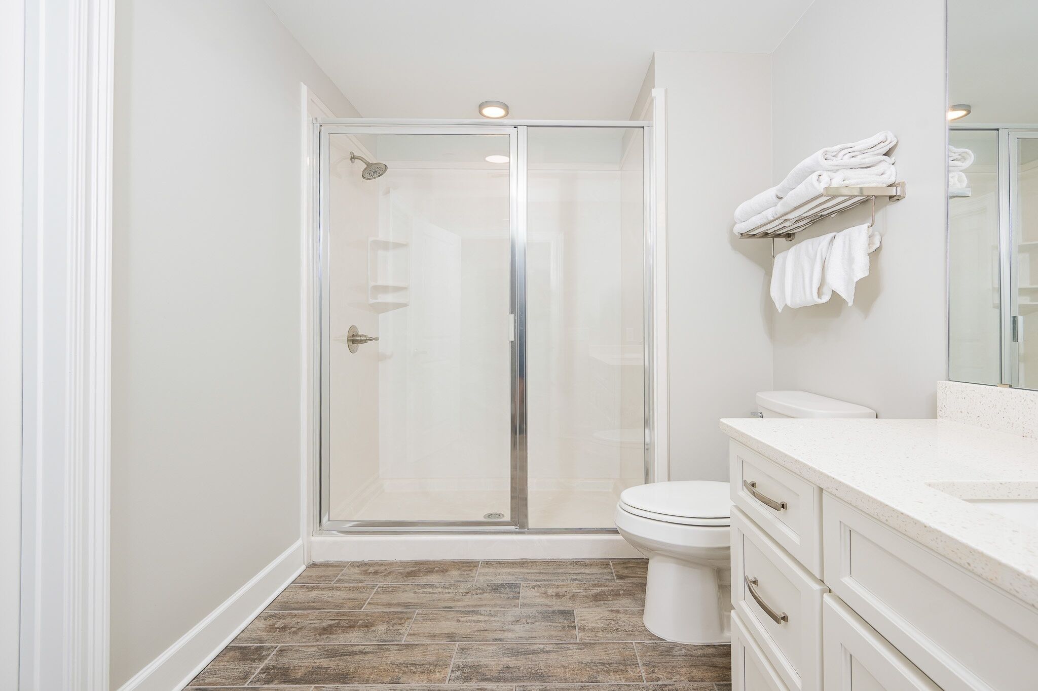 Een moderne badkamer met een douche in een glazen cabine, een wit toilet en een wastafel met een spiegel en een handdoekhouder.