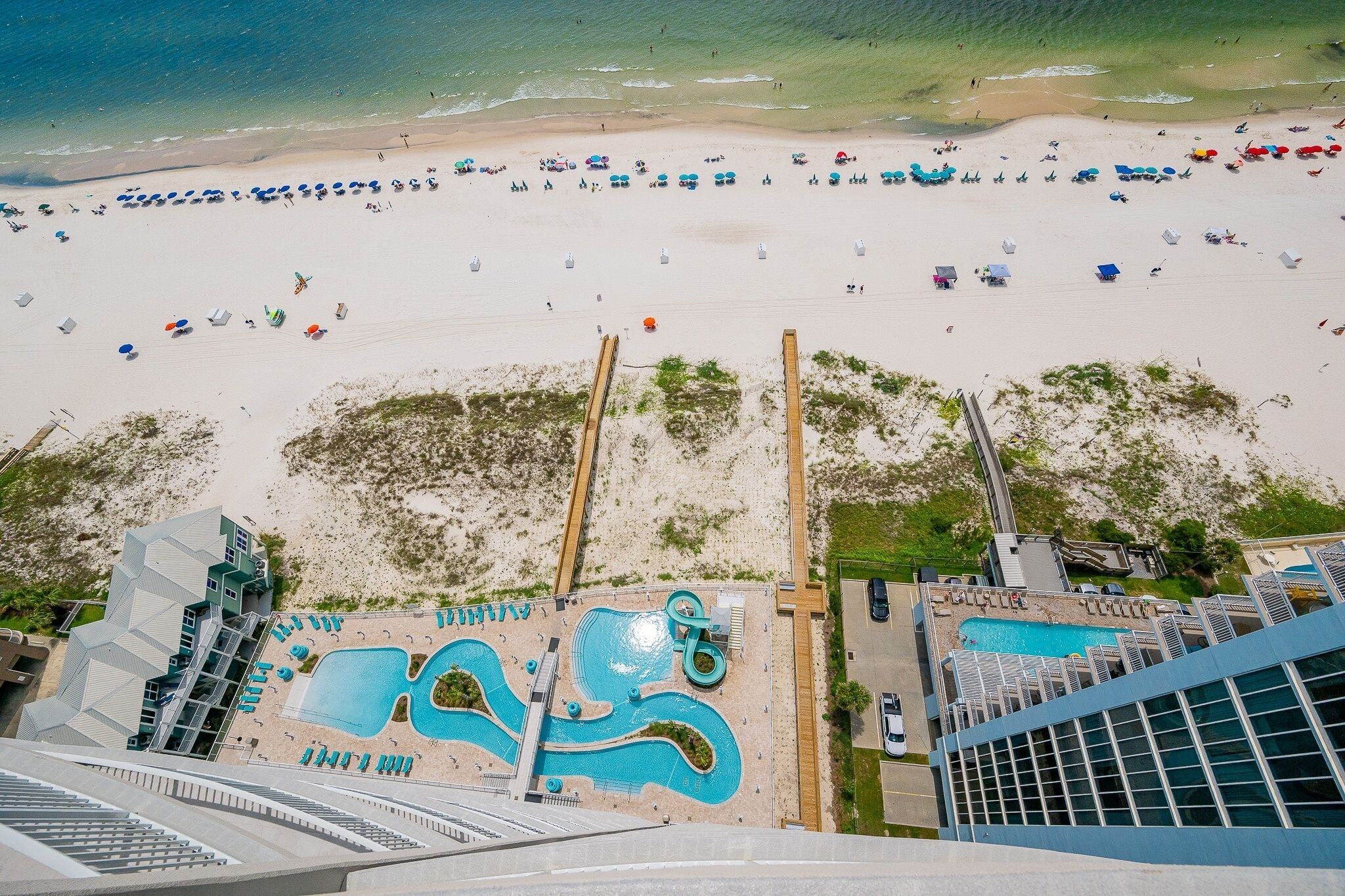 Una playa con numerosas sombrillas y sillas de descanso, una piscina y un paseo marítimo que lleva a la playa.
