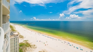 A beach with a pier extending into the ocean, a clear sky, and a view of a hotel building on the left. - Phoenix Gulf Shores Ii 2101 4 Bedroom Condo (Gulf Shores)