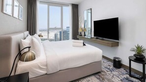 Habitación de hotel con una cama grande, un televisor montado en la pared, una ventana con vistas a la ciudad y una mesita con una planta.