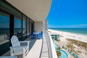 A balcony with white Adirondack chairs, a table, and a pool area with lounge chairs. - Phoenix Gulf Shores Ii 602 3 Bedroom Condo (Gulf Shores)