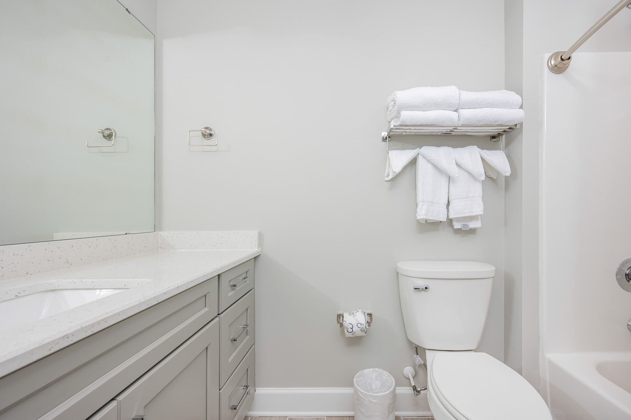 Un baño moderno con un lavamanos, inodoro y bañera blancos. Hay toallas ordenadas en un perchero sobre el inodoro.
