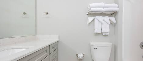 A modern bathroom with a white sink, toilet, and bathtub. There are towels neatly stacked on a rack above the toilet.