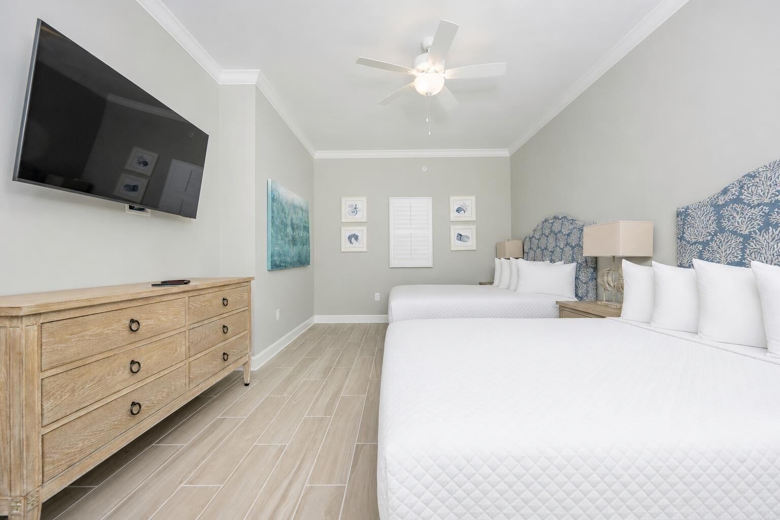 A hotel room with a bed, a TV, a ceiling fan, a wooden dresser, and artwork on the walls.