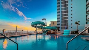 A swimming pool with a water slide, a high-rise building, and a sunset sky. - Phoenix Gulf Shores Ii 2101 4 Bedroom Condo (Gulf Shores)