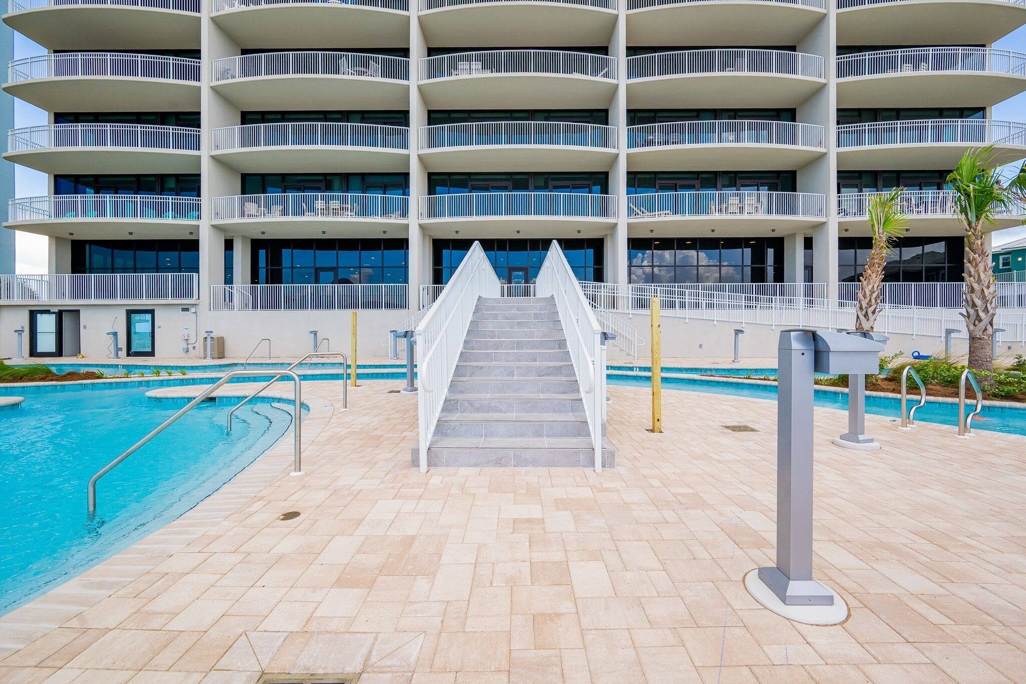 Ein mehrstöckiges Hotel mit Poolbereich, inklusive einer Treppe zum Pool und einer flachen Dachterrasse.