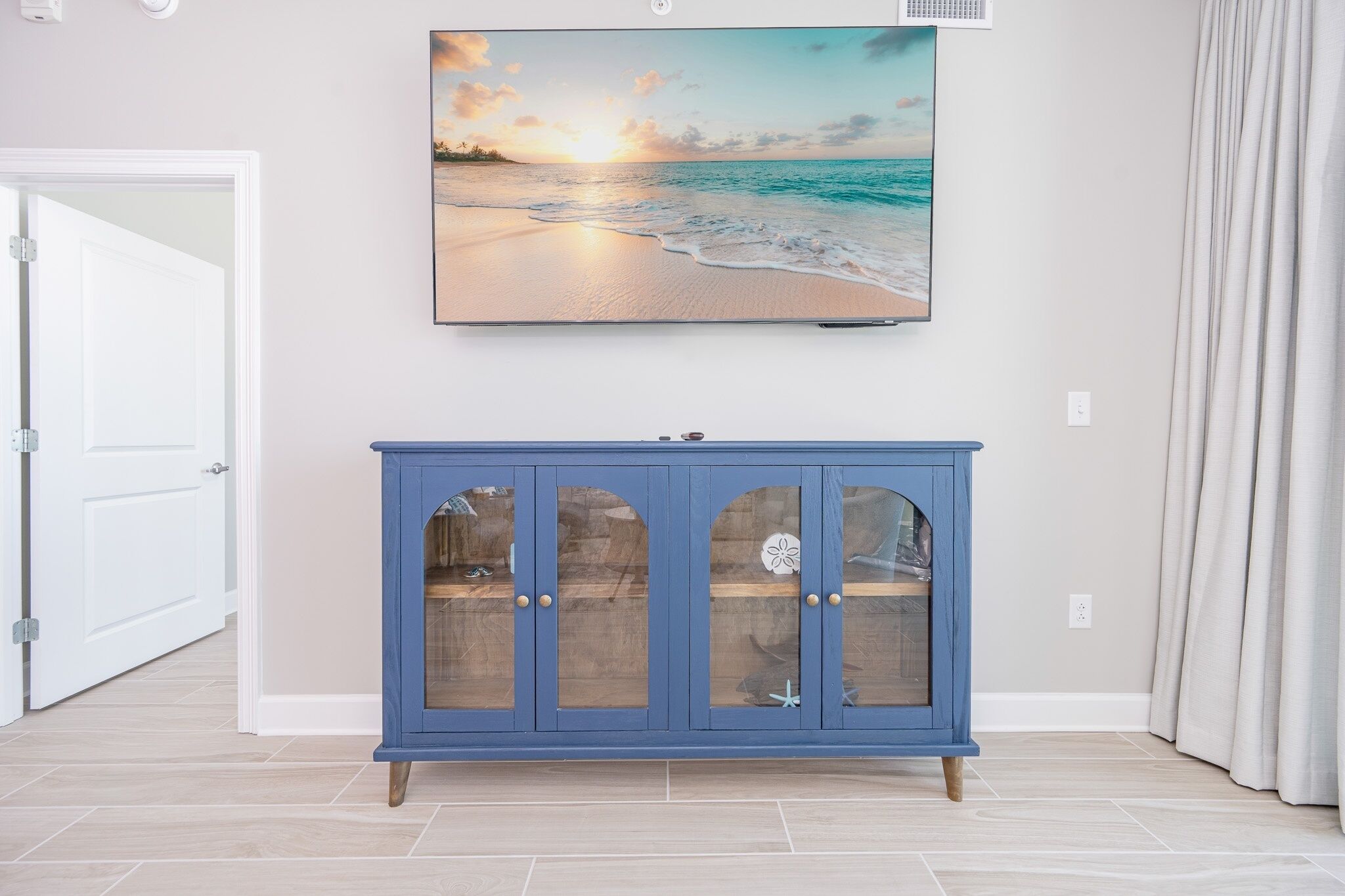 A room with a blue cabinet, a painting of a beach scene, and a white door.