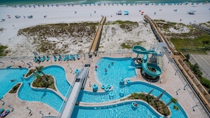 A large outdoor swimming pool with multiple lanes and a water slide, surrounded by beach chairs and umbrellas. - Phoenix Gulf Shores Ii 602 3 Bedroom Condo (Gulf Shores)
