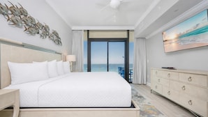 A hotel room with a large bed, a ceiling fan, a TV, a dresser, and a view of the ocean. - Phoenix Gulf Shores Ii 602 3 Bedroom Condo (Gulf Shores)