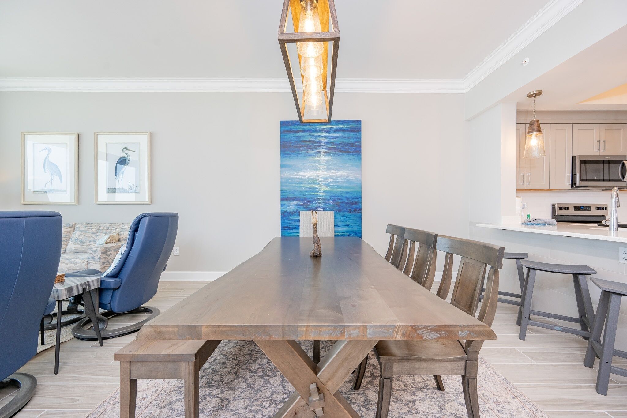 A dining area with a wooden table and chairs, a blue sofa, and a painting of a seascape.