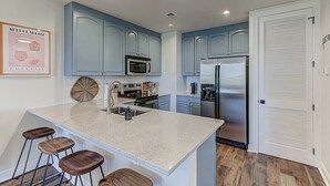 A kitchen with blue cabinets, a stainless steel refrigerator, a microwave, and a bar area with stools.