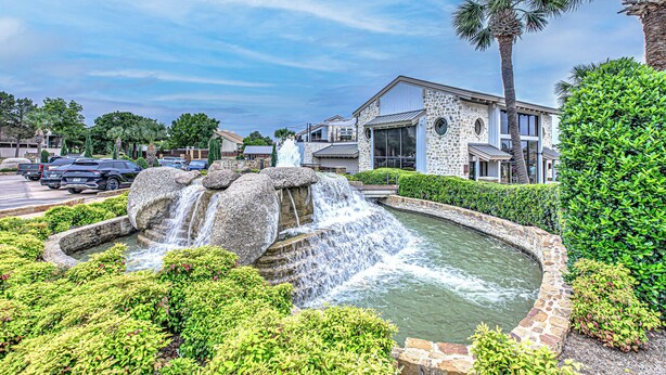A landscaped area with a water feature, stone buildings, and palm trees.