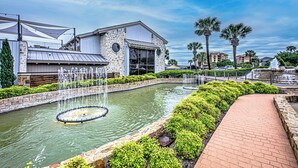 A building with a stone facade, a fountain, and a landscaped area with palm trees.