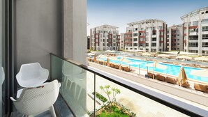 Un balcon avec des chaises blanches et une balustrade en verre donnant sur un espace piscine équipé de chaises longues et de parasols.