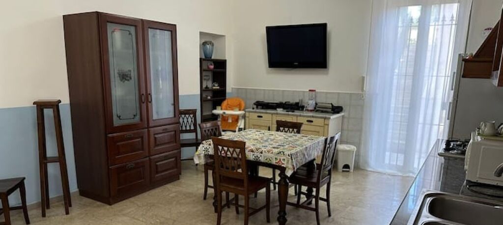 Uma cozinha compacta com mesa, cadeiras, armário, televisão e janela.