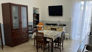 A compact kitchen with a dining table, chairs, a cabinet, a TV, and a window. - GranComfort between Naples and Caserta (Castel Volturno)