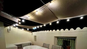 Un espacio para comer al aire libre con una mesa redonda y sillas, un área de estar cubierta y luces colgantes.