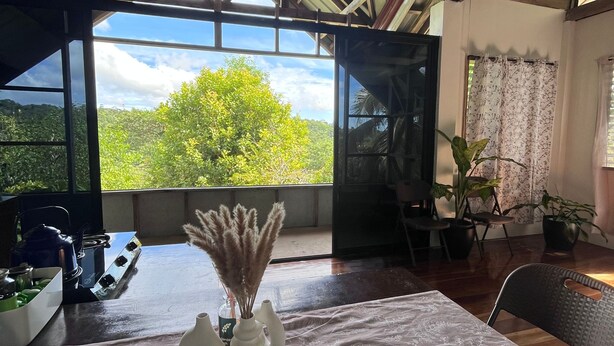 A dining area with a table set for two, a view of the outdoors, and a ceiling with wooden beams. - Siquijor Hilltop House Near Cambugahay Falls (Lazi)