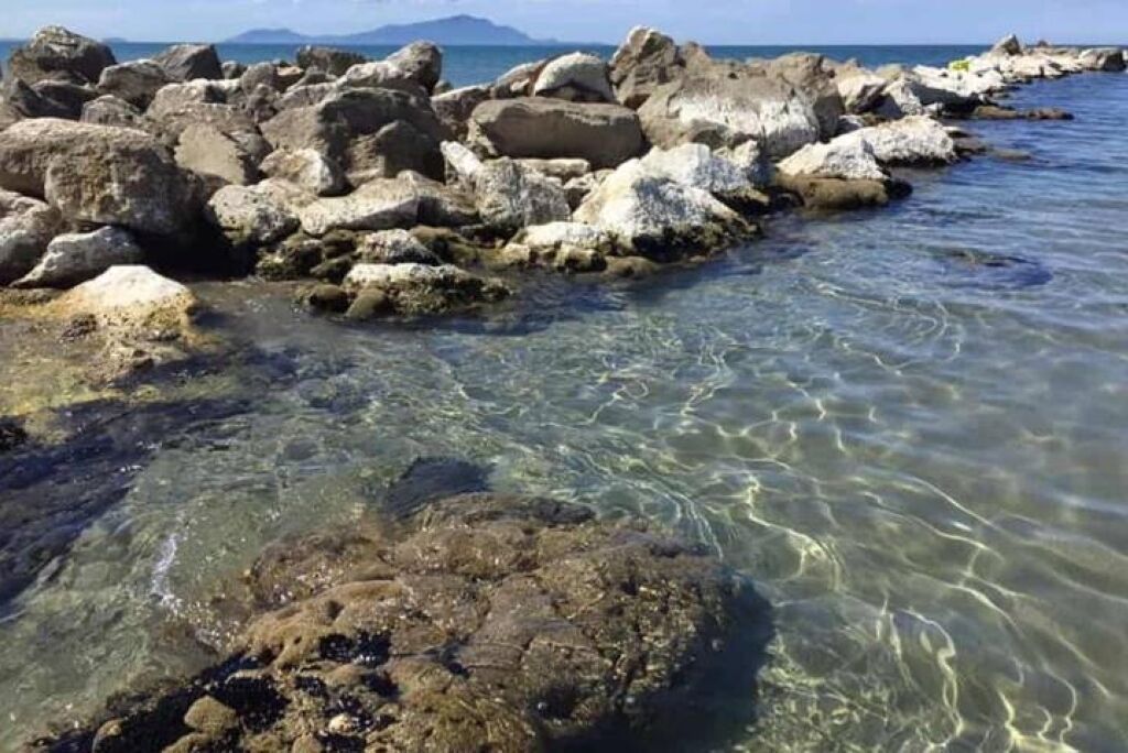 Un littoral rocheux, avec une eau claire et des montagnes qui se dessinent à l’horizon.