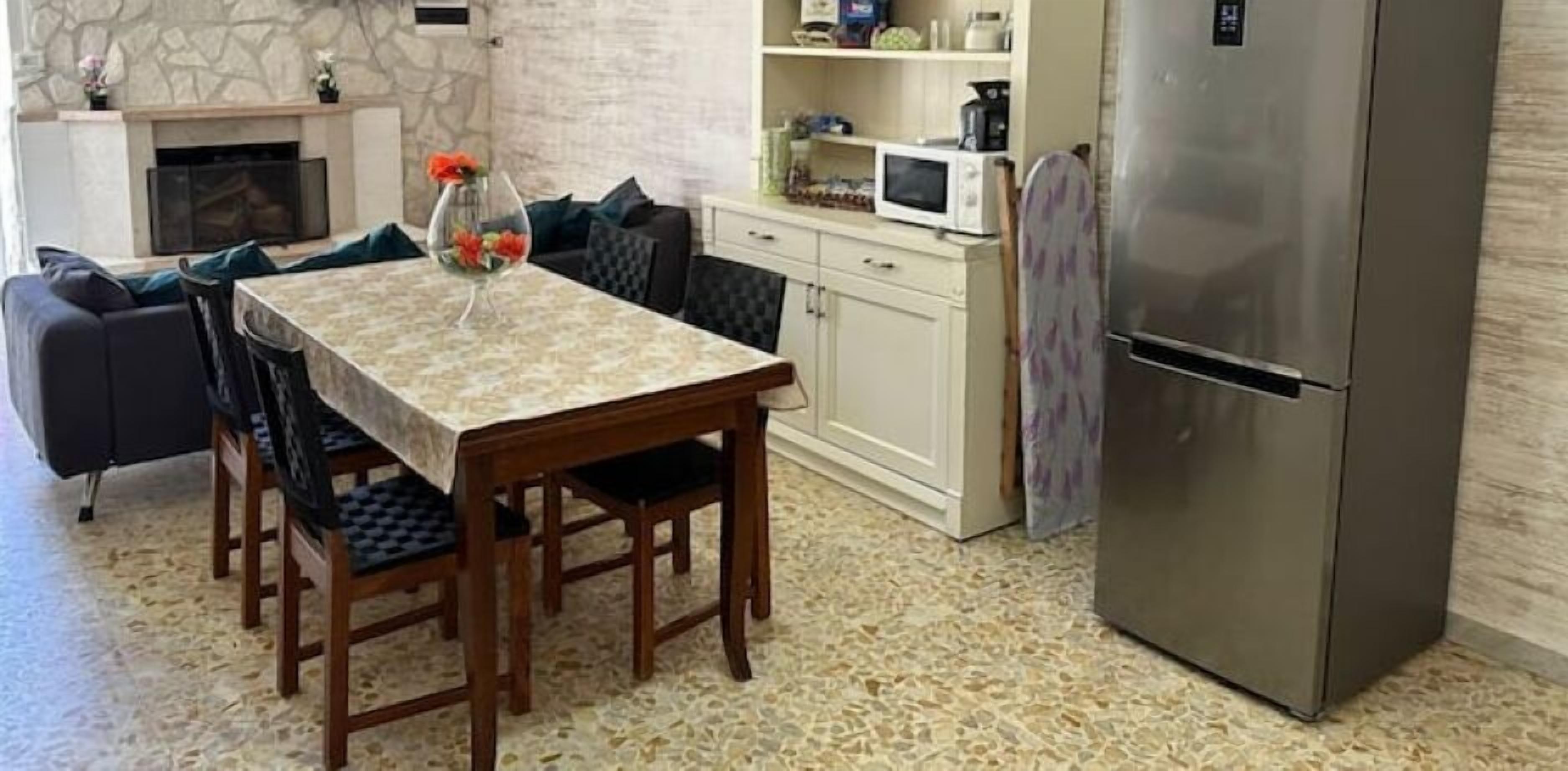 Un comedor con una mesa, sillas, un microondas, un refrigerador y una pared de piedra.