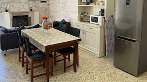 Un comedor con una mesa, sillas, un microondas, un refrigerador y una pared de piedra.