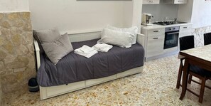 Ein kleines Schlafzimmer mit Bett, einer Küchenzeile und einer Steinwand.