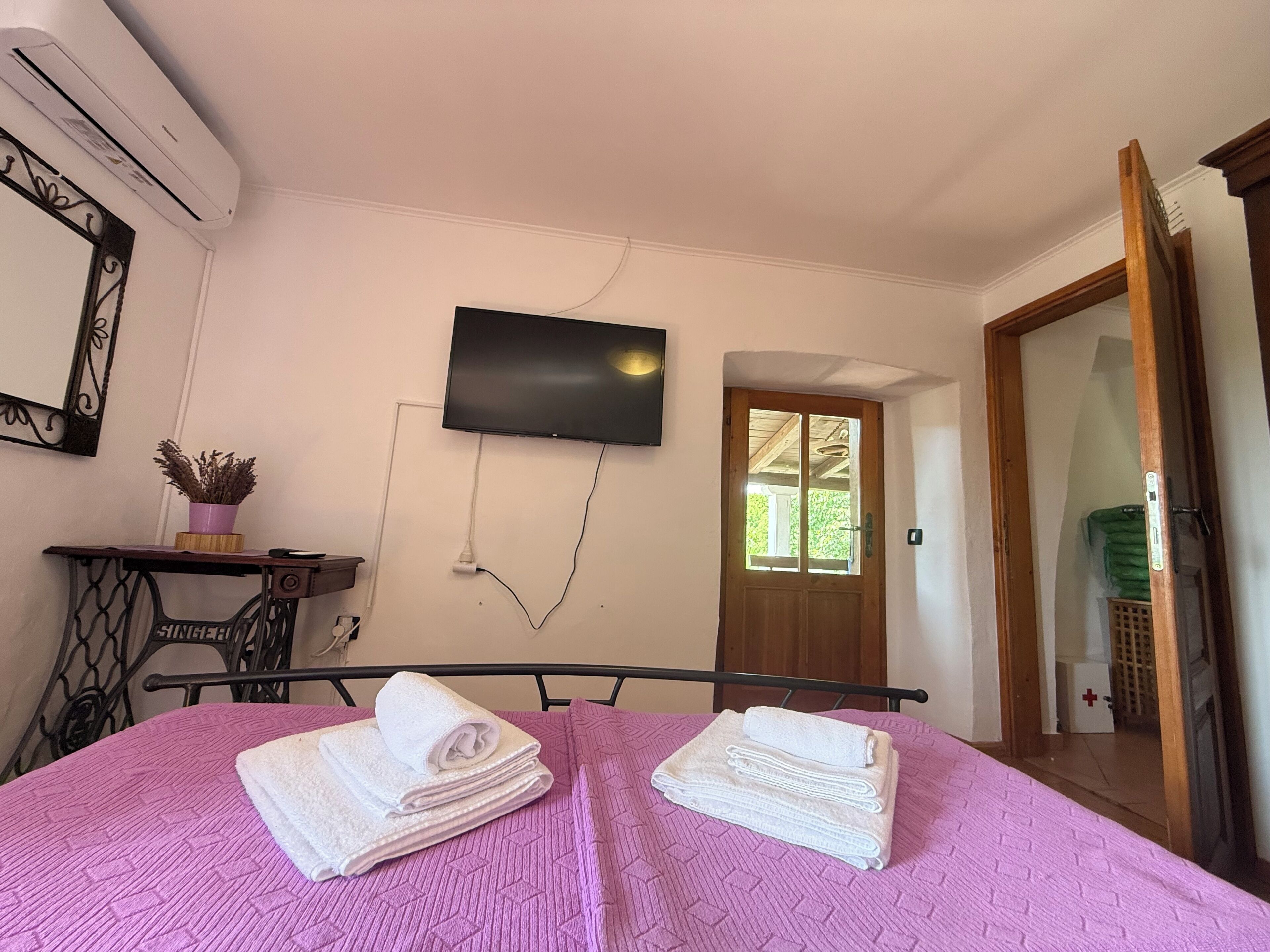 Une chambre à coucher avec un lit, un téléviseur fixé au mur, une machine à coudre et une porte donnant sur une autre pièce.