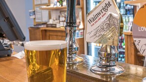 A bar with two taps labeled 'Wainwright The Golden Beer' and a glass of beer on a black coaster. - The Pheasant Inn (Grange-over-Sands)