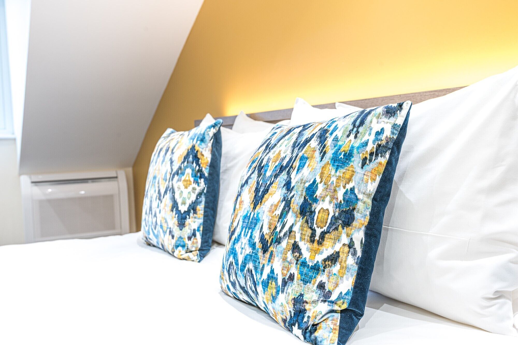 Una camera d'albergo con un letto, cuscini bianchi e un cuscino decorato.