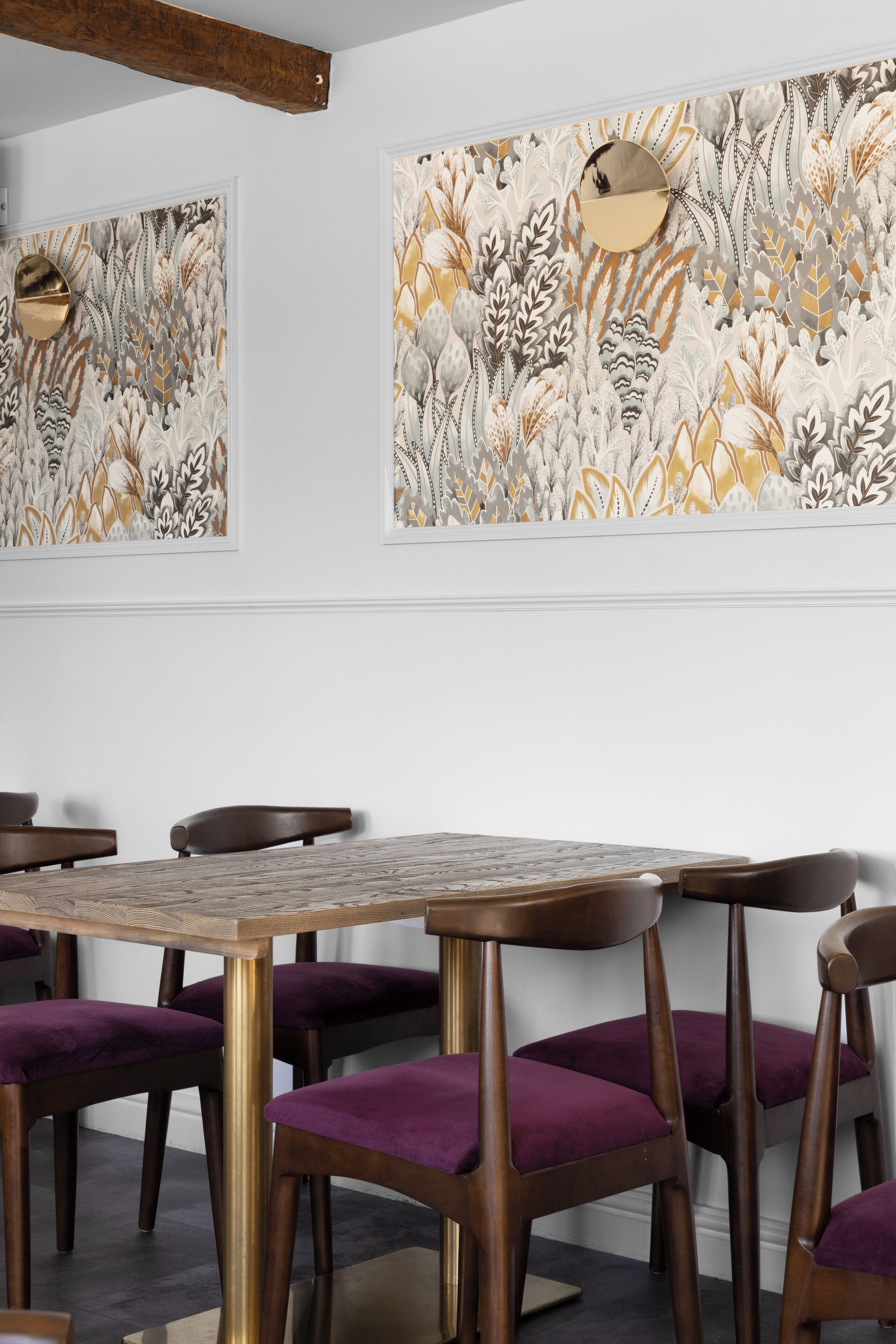 A dining area with a round table and purple upholstered chairs, surrounded by white walls with floral artwork.