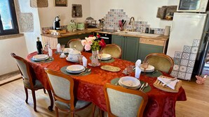 Uma sala de jantar com uma mesa posta para seis, cadeiras, cozinha ao fundo e uma janela.