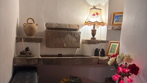 Uma cozinha rústica com pia de pedra, banco de madeira, panela pendurada, vela, luminária e um vaso com flores.