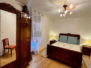 A bedroom with a wooden bed, two bedside lamps, a wooden wardrobe, a chair, and a window with sheer curtains. - Holiday Home 'Angelina' with Wi-Fi (Martrin)