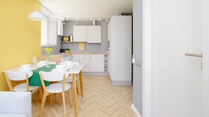 Una cocina moderna con armarios blancos, suelo de madera en espiga y una zona de comedor con mantel verde y sillas blancas.