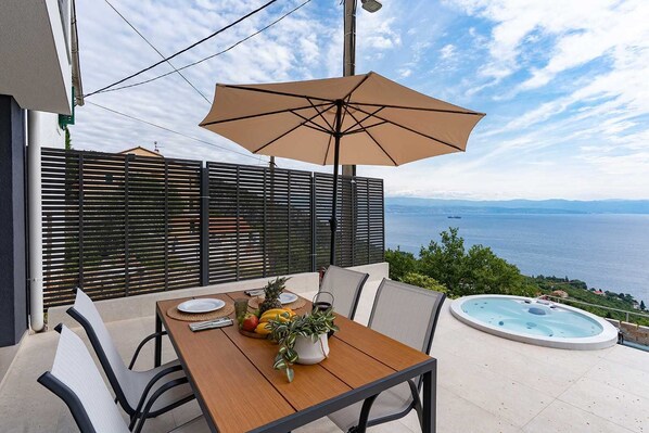 A patio with a table set for two, a hot tub, and a view of the sea.