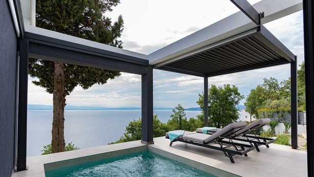 A modern outdoor pool area with a view of the sea, lounge chairs, and a pergola structure.