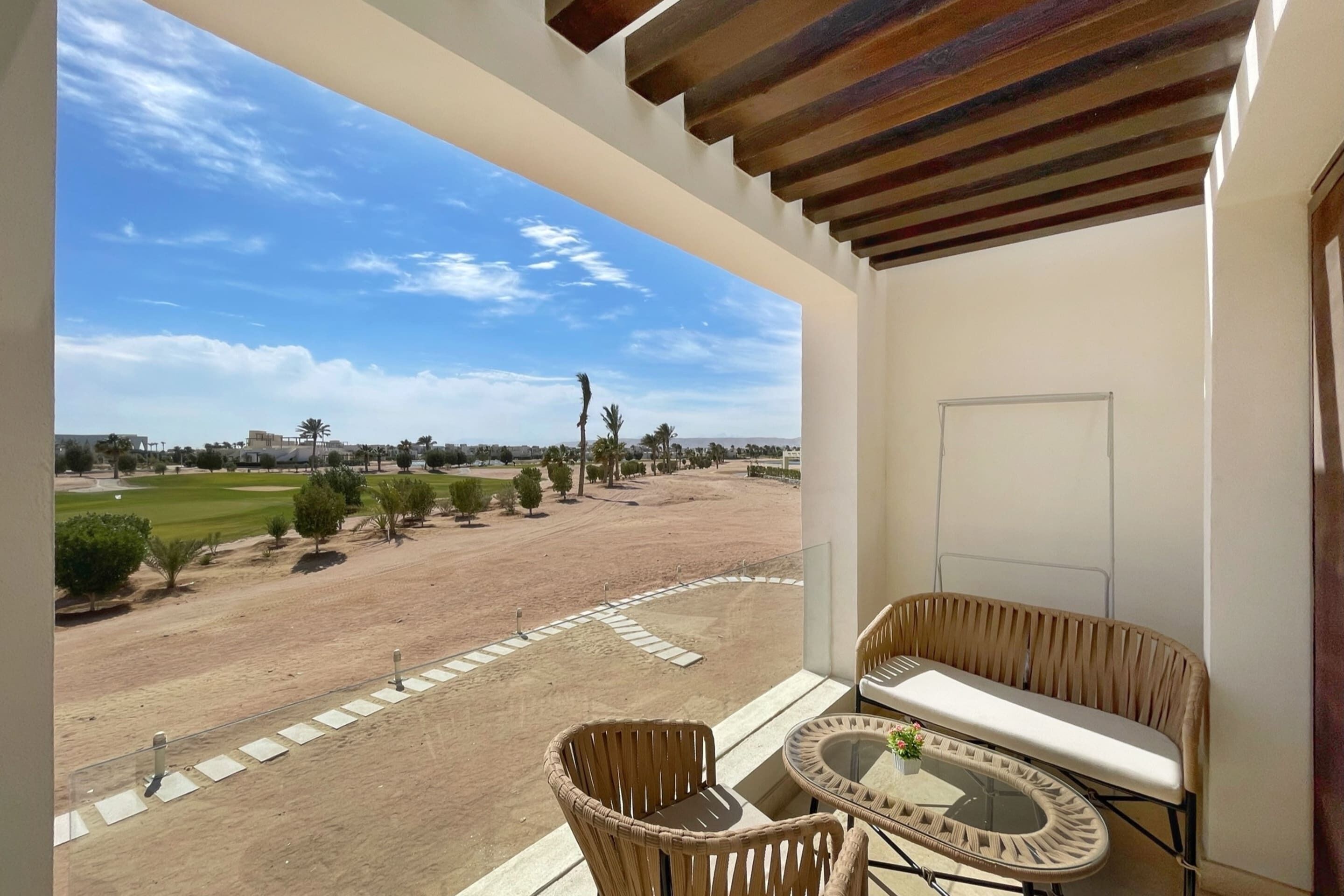 Un balcón con mobiliario de mimbre, una mesa de vidrio y vista a un campo de golf.
