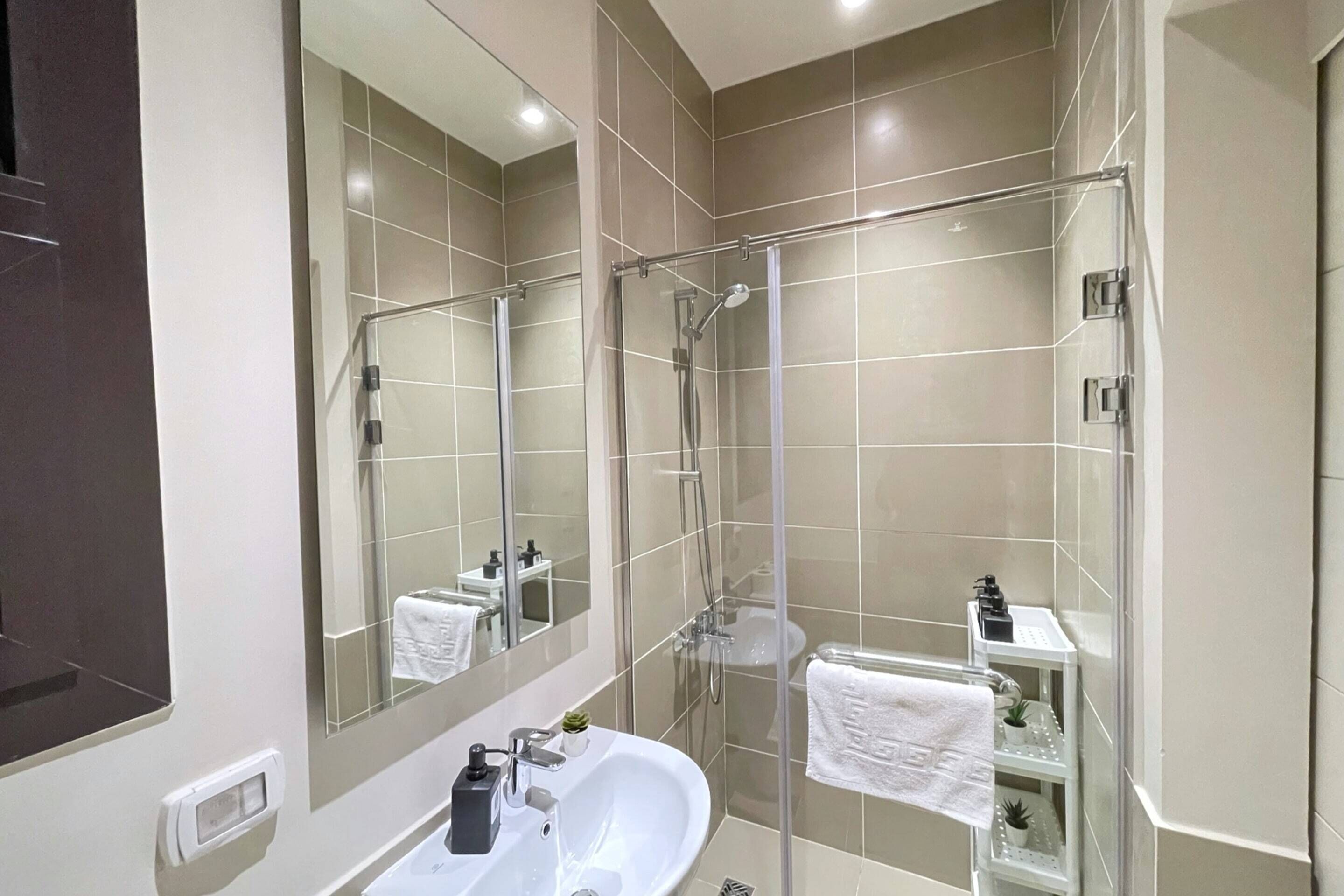 A modern bathroom with a glass-enclosed shower, a white sink, and a large mirror.