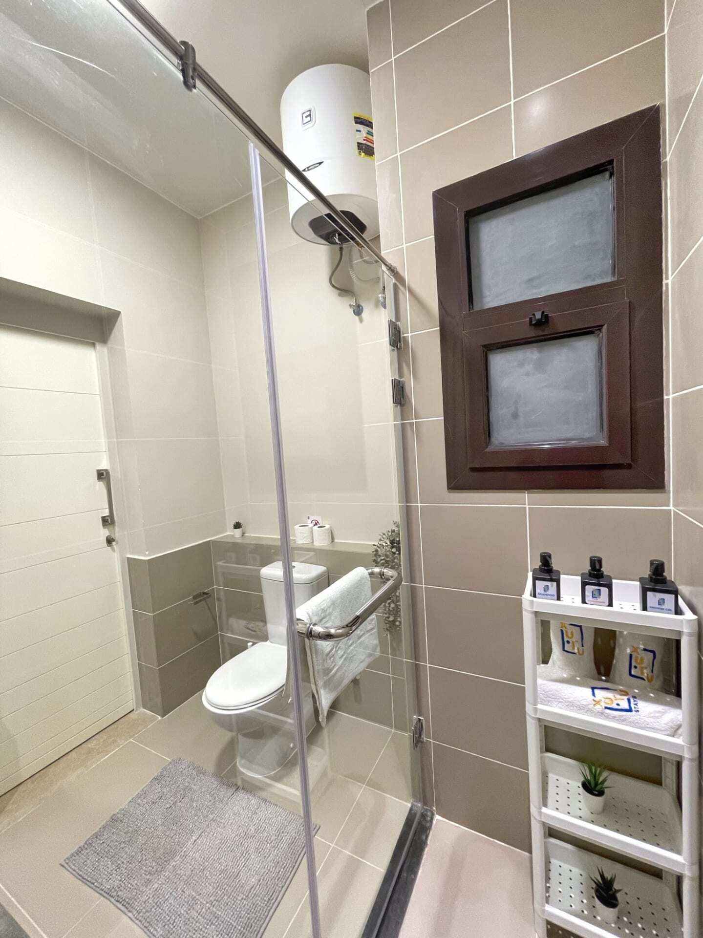 Et moderne badeværelse med et glasafskærmet brusebad, toilet og en hylde med toiletartikler.