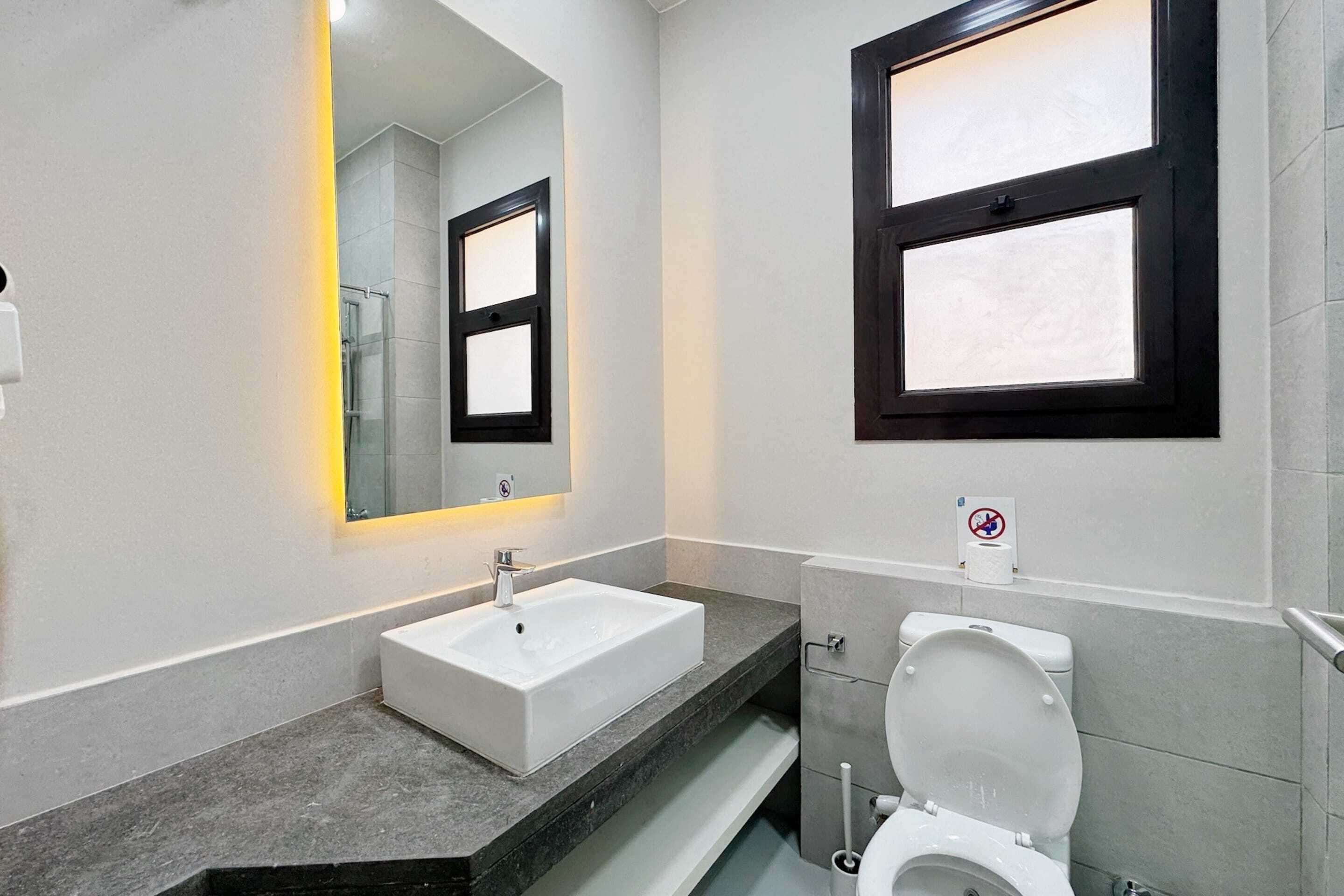 A modern bathroom with a white sink, a mirror with a black frame, and a toilet.