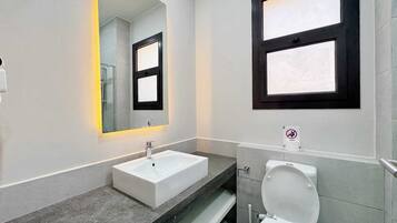 A modern bathroom with a white sink, a mirror with a black frame, and a toilet.