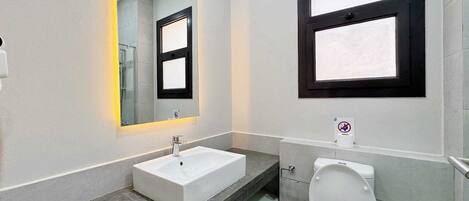 A modern bathroom with a white sink, a mirror with a black frame, and a toilet.